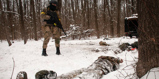 A volunteer of the Ukrainian Territorial Defense Forces looks at a dead body of a soldier lying in a forest in the outskirts of Kharkiv, Ukraine's second-largest city, Monday, March 7, 2022. 