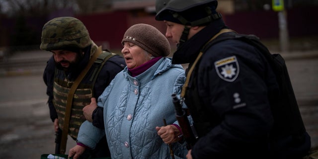 Ukrainian police officers help a woman fleeing as the artillery echoes nearby in Irpin, in the outskirts of Kyiv, Ukraine, Monday, March 7, 2022. 