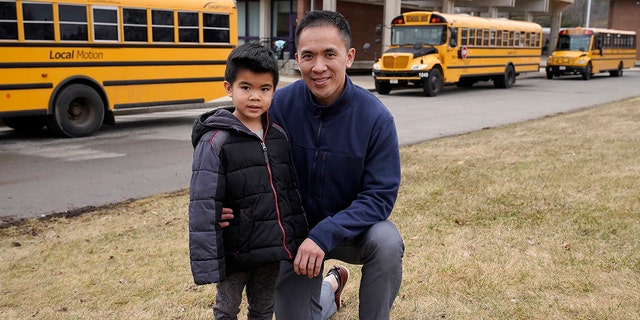 Jason Chan, right, kneels next to his 5-year-old son Skyler, both of Needham, Mass., outside Newman Elementary School, Monday, March 7, 2022, in Needham. Chan said his two school-age children, including Skyler, who has never known schooling without a mask, would be perfectly content wearing them until the end of the school year, if it came down to it. (AP Photo/Steven Senne)