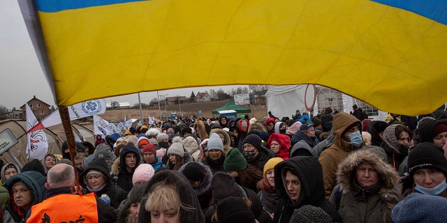 A Ukrainian volunteer Oleksandr Osetynskyi, 44 holds a Ukrainian flag and directs refugees after fleeing from Ukraine and arriving at the border crossing in Medyka, Poland, Monday, March 7, 2022. (AP Photo/Visar Kryeziu)