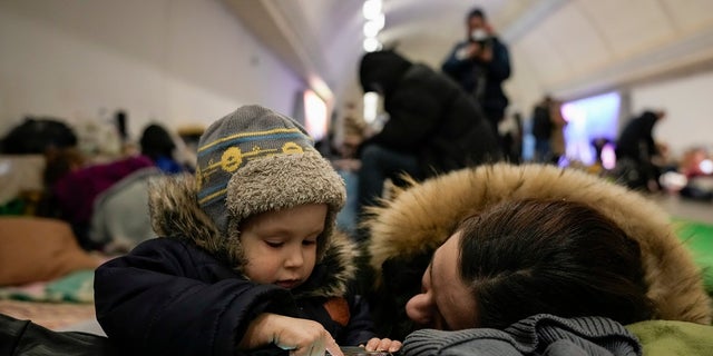 A woman and her child sit on the pavement in a subway station turned into a shelter in Kyiv, Ukraine, on Tuesday. (Associated Press)