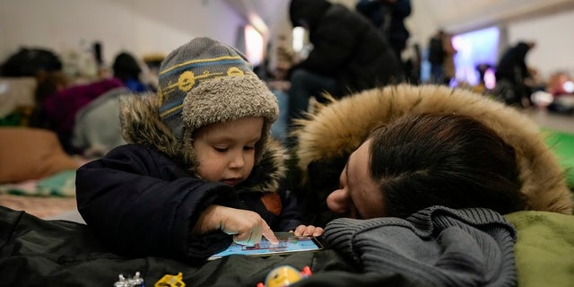 A woman and her child sit on the pavement in a subway station turned into a shelter in Kyiv, Ukraine, on Tuesday. (Associated Press)