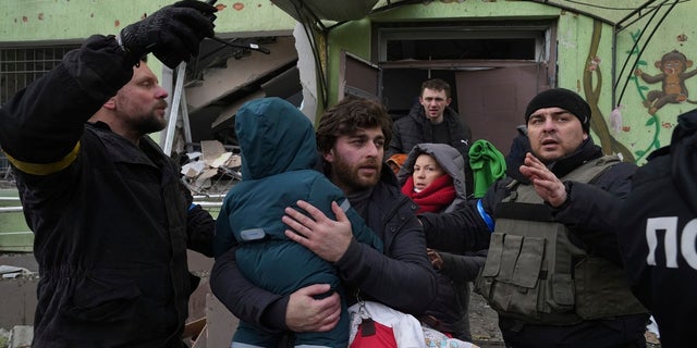 A man carries his child away from the shell-damaged maternity hospital in Mariupol, Ukraine