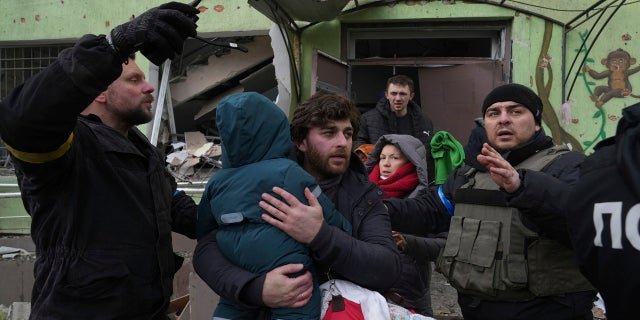 A man carries his child away from the damaged by shelling maternity hospital in Mariupol, Ukraine