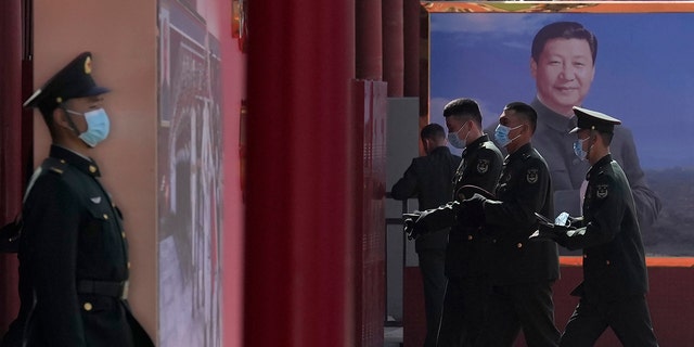 Chinese military personnel pass by a board displaying a photo of Chinese President Xi Jinping on March 4, 2022, in Beijing. 