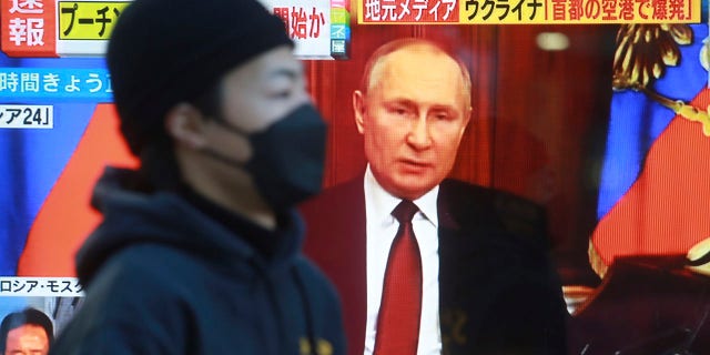 A man walks past a TV screen with an image of Russia's President Vladimir Putin in Tokyo, Thursday, Feb. 24, 2022. As Russia intensifies its assault on Ukraine, it is getting a helping hand from China in spreading inflammatory and unsubstantiated claims that the U.S. is financing biological weapons labs in Ukraine.