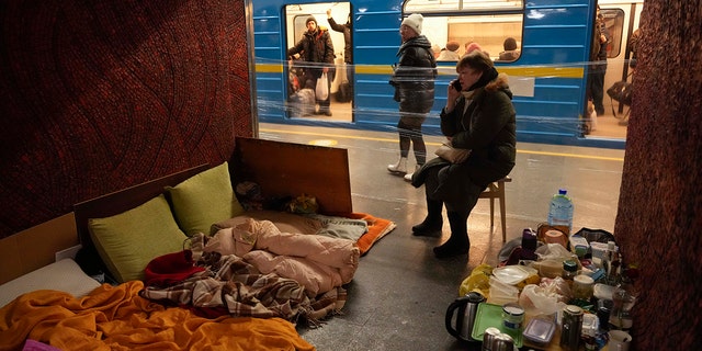 Una mujer con sus pertenencias y comida, sentada en una silla en un refugio improvisado en un metro que los residentes de la ciudad usan como refugio antiaéreo mientras pasa un tren en la línea opuesta en Kiev, Ucrania, el domingo 13 de marzo de 2022.