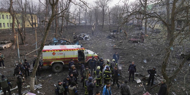 Ukrainian servicemen and firefighters stand in the area outside a maternity hospital damaged in a shelling attack in Mariupol, Ukraine, Wednesday, March 9, 2022. 