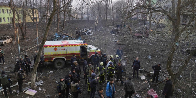 Ukrainian servicemen and firefighters stand in the area outside a maternity hospital damaged in a shelling attack in Mariupol, Ukraine, Wednesday, March 9, 2022.