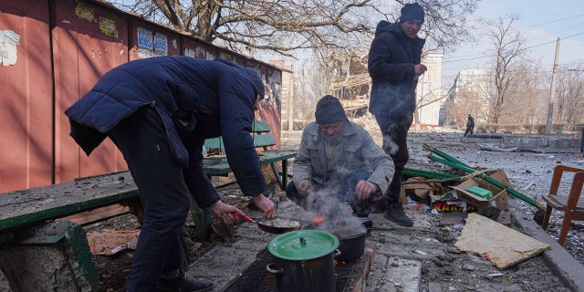 Men cook a meal in a street in Mariupol, Ukraine, Sunday, March 13, 2022. The surrounded southern city of Mariupol, where the war has produced some of the greatest human suffering, remained cut off despite earlier talks on creating aid or evacuation convoys. (AP Photo/Evgeniy Maloletka)