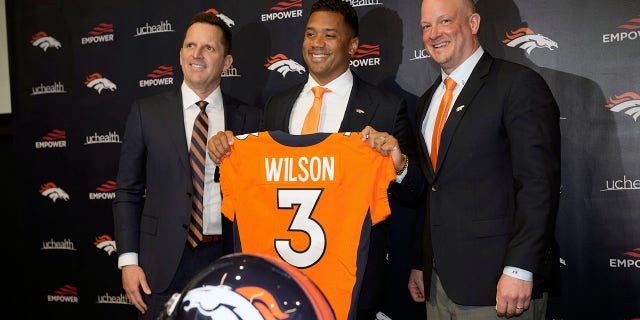 O novo quarterback do Denver Broncos, Russell Wilson, no centro, após o técnico Nathaniel Hockett, o direito e o general manager George Patton na quarta-feira, 16 de março de 2022, após uma coletiva de imprensa na sede da equipe em Englewood, Colorado. 