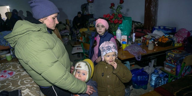 A woman and children taken refuge in a school bomb shelter in Sartana village, which is under the control of the Government of the Donetsk People's Republic, some 11 miles northeast of Mariupol, Ukraine, on March 16, 2022. 