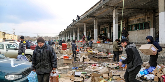 Les résidents locaux transportent de l'eau de l'entrepôt alimentaire, sur le territoire sous le contrôle du gouvernement de la République populaire de Donetsk, à la périphérie de Marioupol, en Ukraine, le vendredi 18 mars 2022.