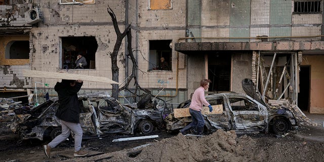 People carry wooden boards to cover the windows of a building damaged by a bombing the previous day in Kyiv, Ukraine, Monday, March 21, 2022. 