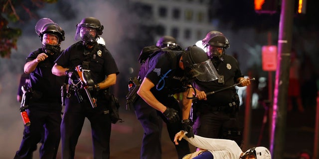 Denver Police Department officers clear a man who fell to the street after they used tear gas and rubber bullets to disperse a protest outside the State Capitol over the death of George Floyd on May 28, 2020, in Denver. 