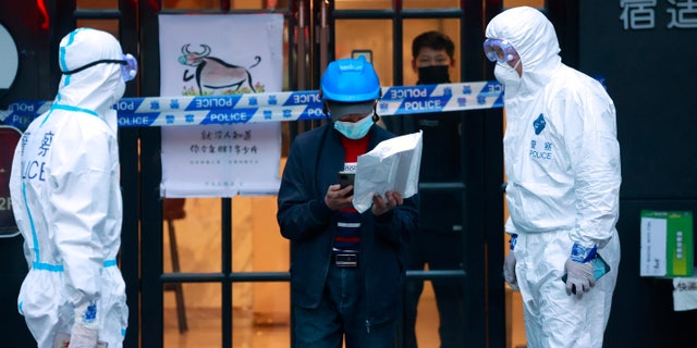 A delivery man walks by police officers with protective suit outside of a hotel in Shanghai, Sjina, op Maart 15, 2022.