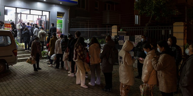 Residents wearing face masks to help protect from the coronavirus line up outside a supermarket at night to buy groceries on Sunday, Maart 27, 2022, in Shanghai, Sjina. 