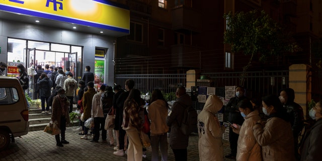 Residents wearing face masks to help protect from the coronavirus line up outside a supermarket at night to buy groceries on Sunday, Maart 27, 2022, in Shanghai, Sjina.