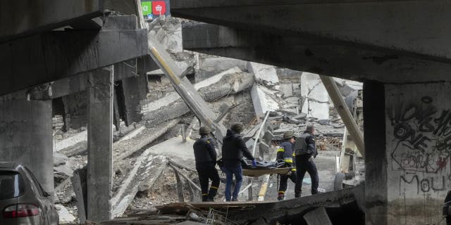 Ukrainian soldiers carry a body of a civilian killed by Russian forces under a destroyed bridge in Irpin near Kyiv, Ukraine, Thursday, March 31, 2022.