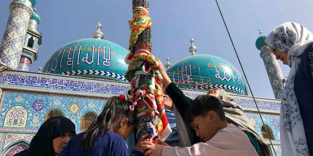 Afghan Shiite children and women kiss the holy mace for blessings during celebrations of Nowruz, the Persian new year, as Taliban soldiers stand guard at the Kart-e-Sakhi shrine in Kabul, Afghanistan, Monday, March 21, 2022. 