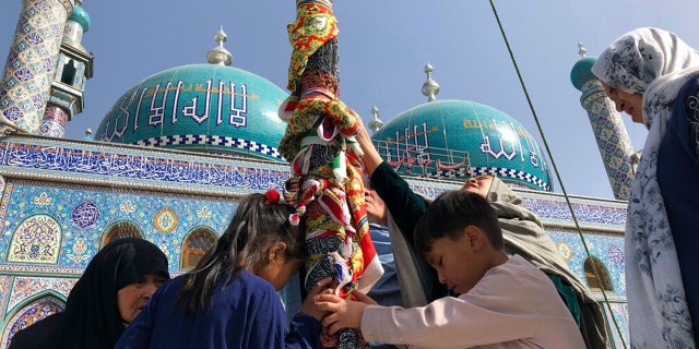 Afghan Shiite children and women kiss the holy mace for blessings during celebrations of Nowruz, the Persian new year, as Taliban soldiers stand guard at the Kart-e-Sakhi shrine in Kabul, Afghanistan, Monday, March 21, 2022.