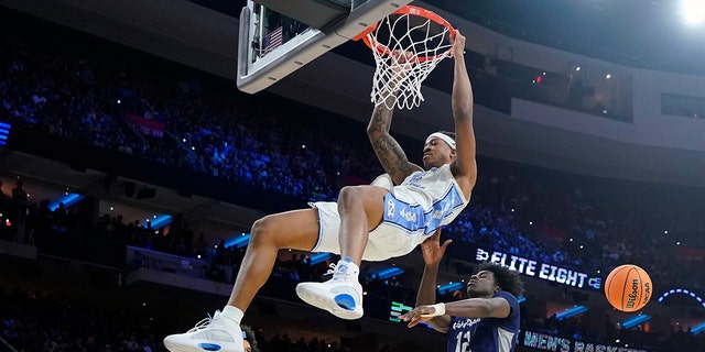 North Carolina's Armando Bacot, left, hangs on the rim after a dunk past St. Peter's Clarence Rupert during the first half of a college basketball game in the Elite 8 round of the NCAA tournament, Sunday, March 27, 2022, in Philadelphia. 