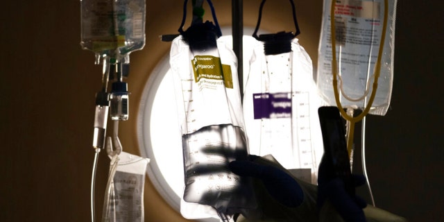 A nurse checks an IV fluid while talking to a COVID-19 patient at Providence Holy Cross Medical Center in Los Angeles