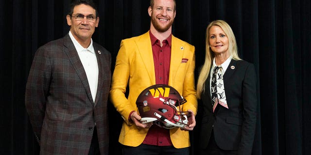 Washington Commanders NFL football team new quarterback Carson Wentz is flanked by team co-owner and co-CEO Tanya Snyder and head coach Ron Rivera as they pose for a picture after Wentz was introduced during a news conference in Ashburn, Va., Thursday, March 17, 2022.