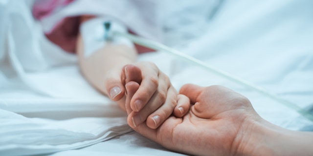 Person holding a hospital patient's hand.