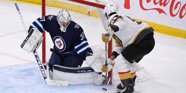Winnipeg Jets goaltender Connor Hellebuyck (37) makes a save on Vegas Golden Knights' Keegan Kolesar (55) during the third period of an NHL hockey game in Winnipeg, Manitoba, Tuesday, March 22, 2022.