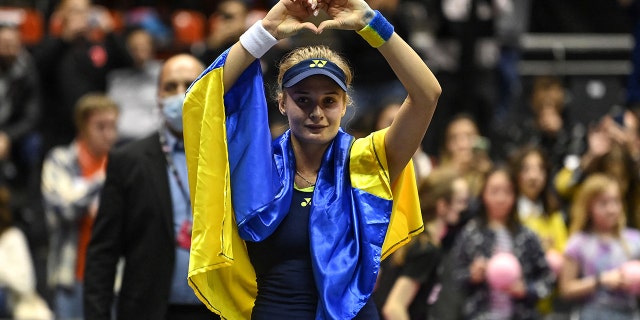 Ukraine's Dayana Yastremska, wrapped in the Ukrainian national flag, reacts at the end of the WTA 6eme Sens Open semi-final tennis match against Romania's Sorana Cirstea in Lyon, on March 5, 2022.