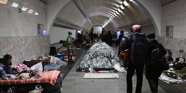 TOPSHOT - Civilians walk by Ukraine residents who use an underground metro station as bomb shelter in Kyiv on March 2, 2022. - On the seventh day of fighting in Ukraine Russia claims control on March 2, 2022 of the southern port city of Kherson, street battles rage in Ukraine's second-biggest city Kharkiv, and Kyiv braces for a feared Russian assault.  (Photo by Aris Messinis / STF / AFP) 