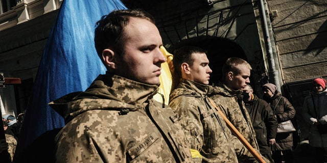 Ukrainian soldiers lead the funeral procession for comrades from the church to the hearses as onlookers hold flowers and watch, in Lviv, March 2022.
