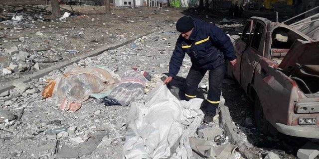 A man covers a dead body after a residential building is hit by a Russian attack in Chernihiv, Ukraine.