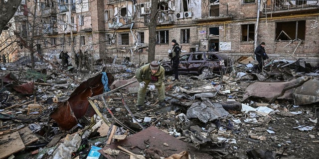Ukrainian servicemen stand next to a damaged building in a residential area after shelling kyiv on March 18, 2022, as Russian troops attempt to encircle the Ukrainian capital as part of their slow-moving offensive.