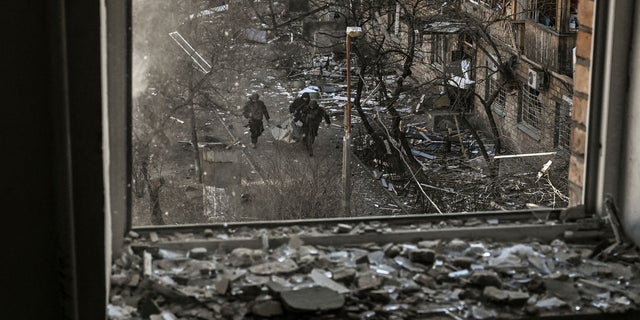 Ukrainian soldiers seen through a building window carrying the remains of a missile after shelling in a residential area in Kiev, March 18, 2022.
