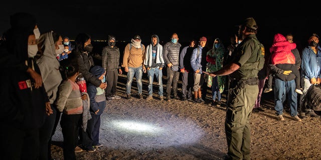 A Border Patrol agent speaks with immigrants before transporting some of them to a processing center on Dec. 9, 2021, in Yuma, Arizona.