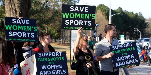 Protesters hold signs before the 2022 NCAA Division I women's swimming and diving championship at the McAuley Aquatic Center on the campus of the Georgia Institute of Technology March 17, 2022, in Indianapolis.