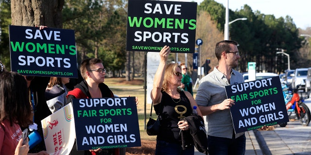 Protesters hold signs before the 2022 NCAA Division I women's swimming and diving championship at the McAuley Aquatic Center on the campus of the Georgia Institute of Technology March 17, 2022, in Indianapolis.