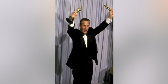 Dances with Wolves director Kevin Costner holds Oscars in the air after winning Academy awards