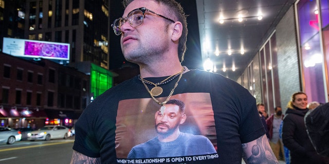 Stephen Coughlin, 31, shows off his custom-made shirt calling attention to the incident between comedian Chris Rock and actor Will Smith from the Oscars as he waited in line to see Rock perform at The Wilbur Theatre in Boston, Massachusetts on March 30, 2022.