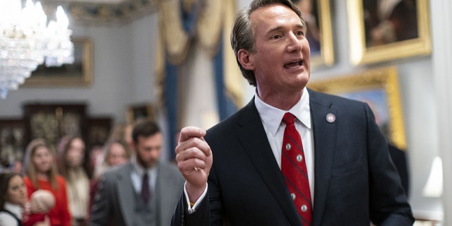 Glenn Youngkin speaking to the press in early 2022 wearing a dark gray suit and red tie