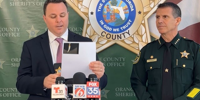 Joe Covelli, a Homicide Sergeant at the Orange County Sheriff's Office holds up a picture of the necklace during a press conference on Thursday.