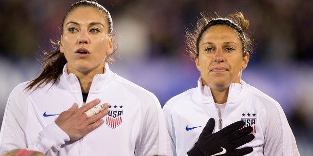 USA goalkeeper Hope Solo (left), and teammate Carli Lloyd during team national anthems before the USA vs. Colombia Women's International friendly football match at the Pratt & Whitney Stadium on April 6, 2016, in East Hartford, Connecticut.