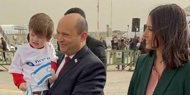 Israel’s Prime Minister, Naftali Bennett, holds a child who made it safely out of Ukraine amid the war; Bennett is accompanied by his wife, Gilat Bennett. 