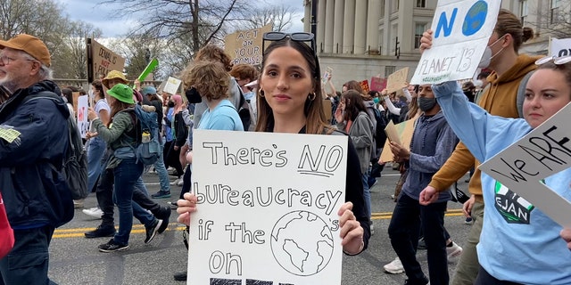 Climate activist holds "there's no bureaucracy if the world is on fire" sign as she marches toward the U.S. Capitol.