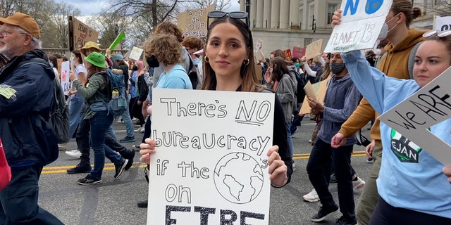 Climate activist holds "there's no bureaucracy if the world is on fire" sign as she marches toward the U.S. Capitol.