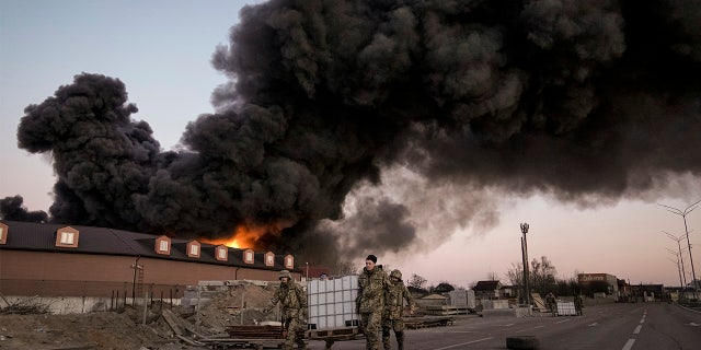 Ukrainian service members carry containers backdropped by a blaze at a warehouse after a bombing on the outskirts of Kyiv, Ukraine, Thursday, March 17, 2022.