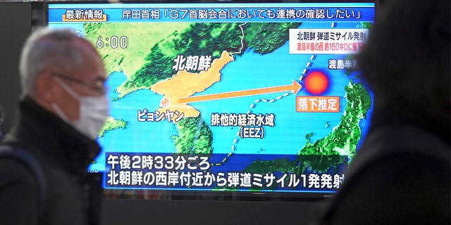 Pessoas caminham por uma calçada em frente a uma TV que exibe um programa de notícias sobre o lançamento de míssil da Coreia do Norte na quinta-feira, 24 de março de 2022, em Tóquio.