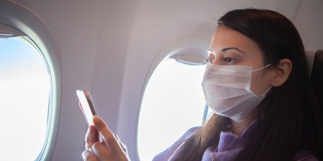 A woman wearing a mask sits on a plane